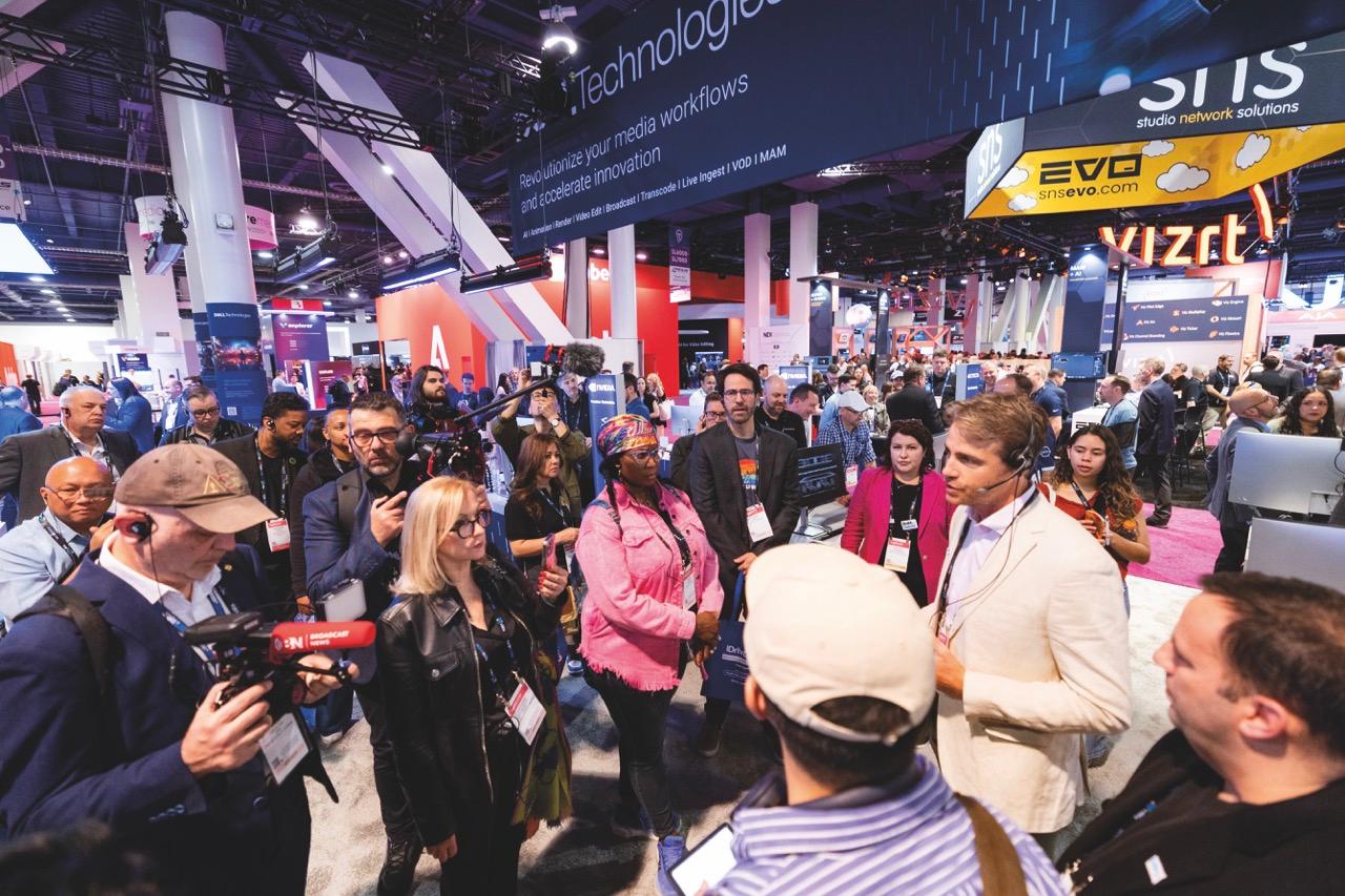 A crowd watching a man with a headset talk as he is filmed at a conference hall
