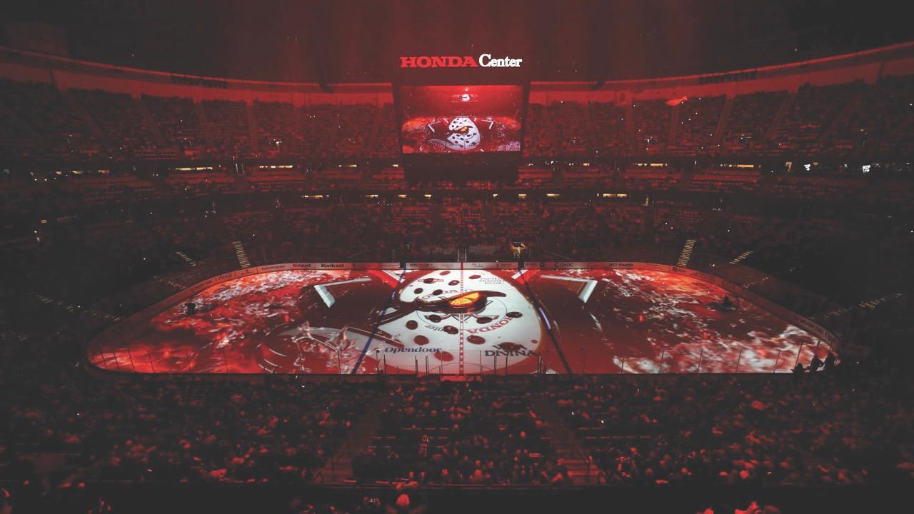 A basketball cool lit in red with a projection on the court and a packed audience