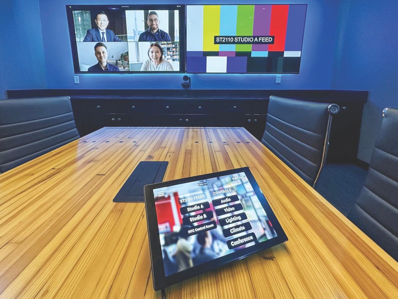 A tablet on a wooden table in an office room with a screen at the end of the table