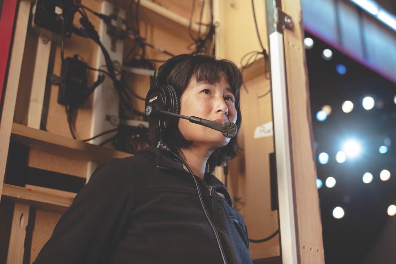 A woman wearing a headset standing by the side of a stage