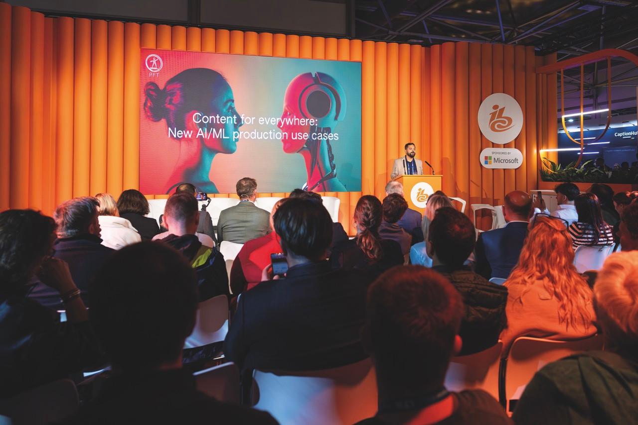 The IBC conference with a man speaking at a stand at the front of an orange room