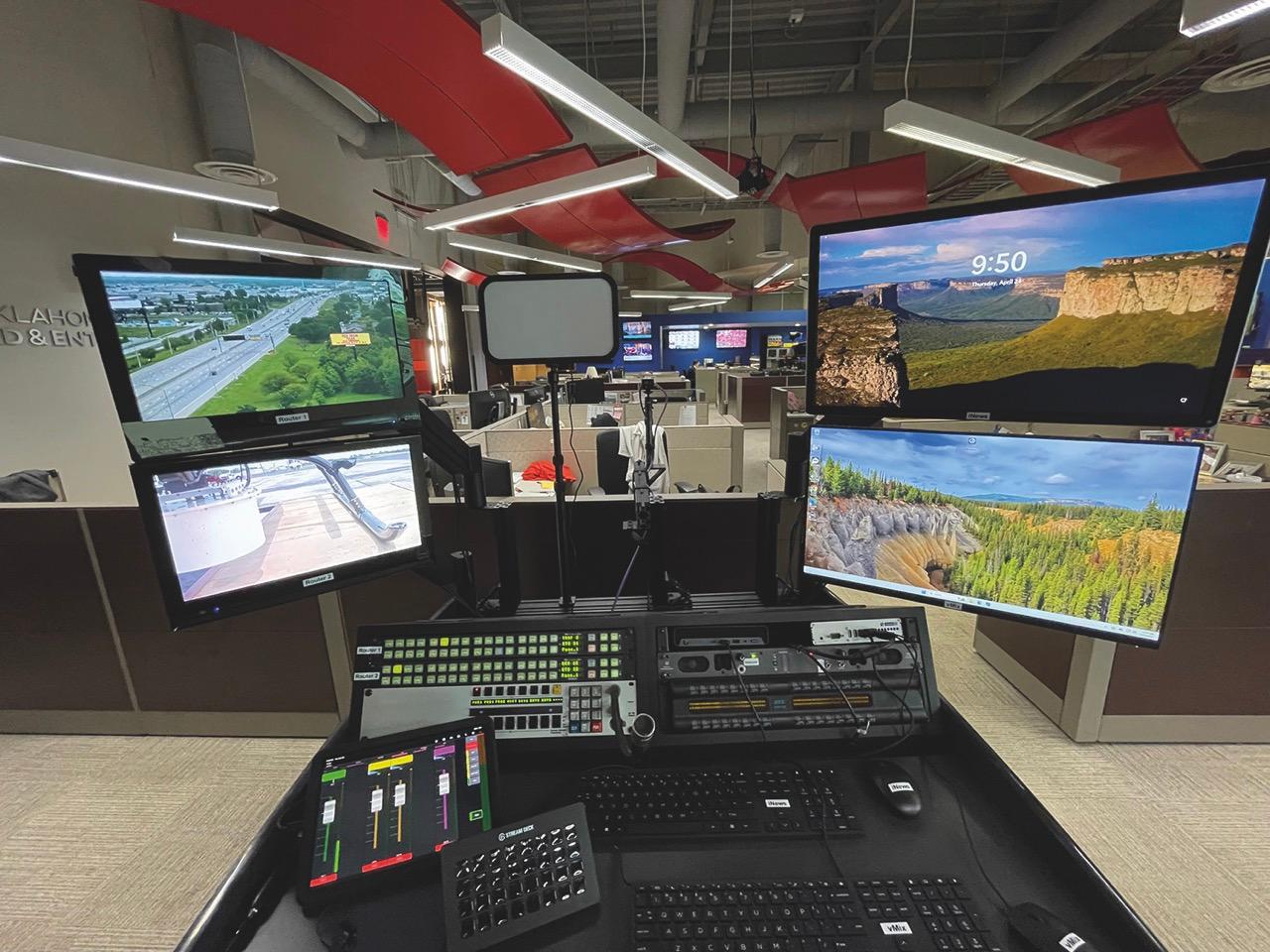 A mixing desk with monitors showing landscapes at the back of a newsroom