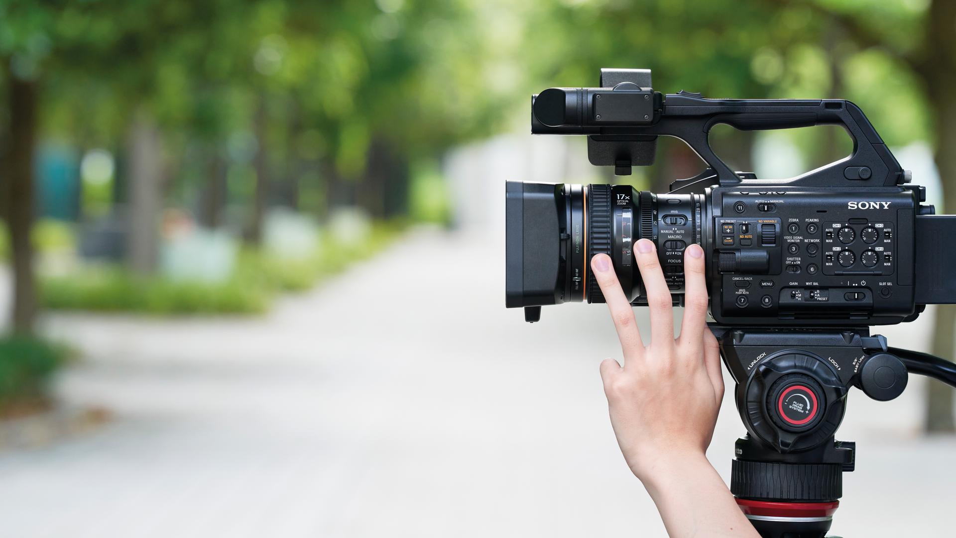Side view of a professional Sony camera with a hand adjusting the buttons. A blurred path in the background