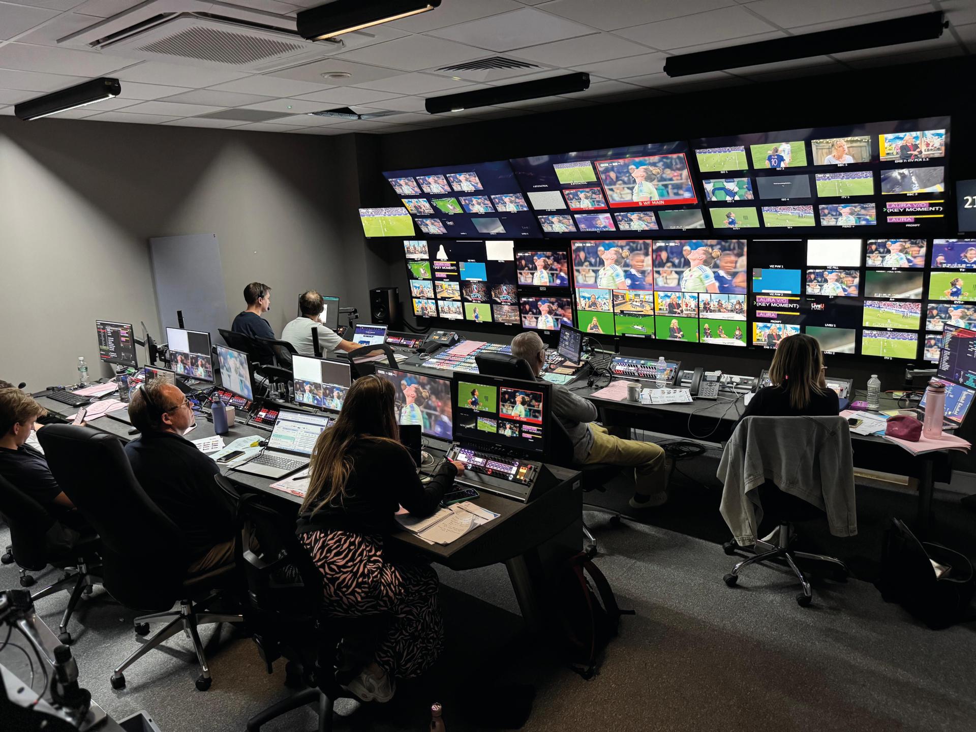 A mixing studio with people working at desks and looking at a wall of screens
