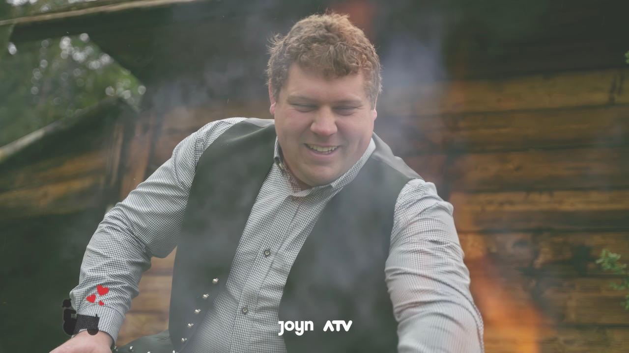 A man in a waistcoat smiles and stokes a fire