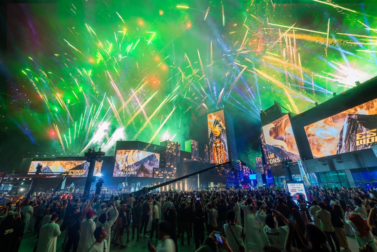 An arena for the Esports World Cup filled with people, screens and green lighting