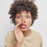 Close up shot of a woman who keeps her hand near her mouth and whispers information