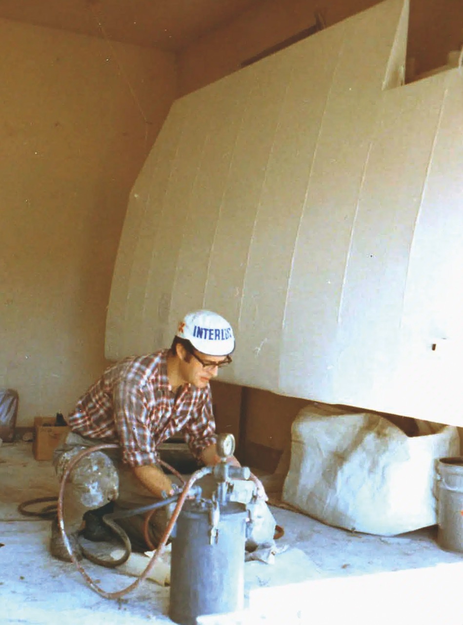 A man knelt down constructing an airplane wing on the floor of a garage