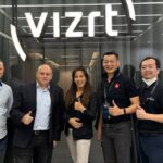 Five people stand smiling in front of a glass wall with a sign that says "Vizrt"