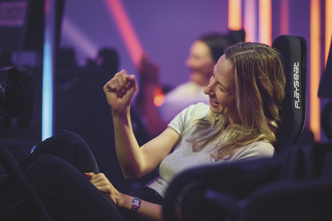 A woman sitting in a gaming chair celebrating a victory in esports