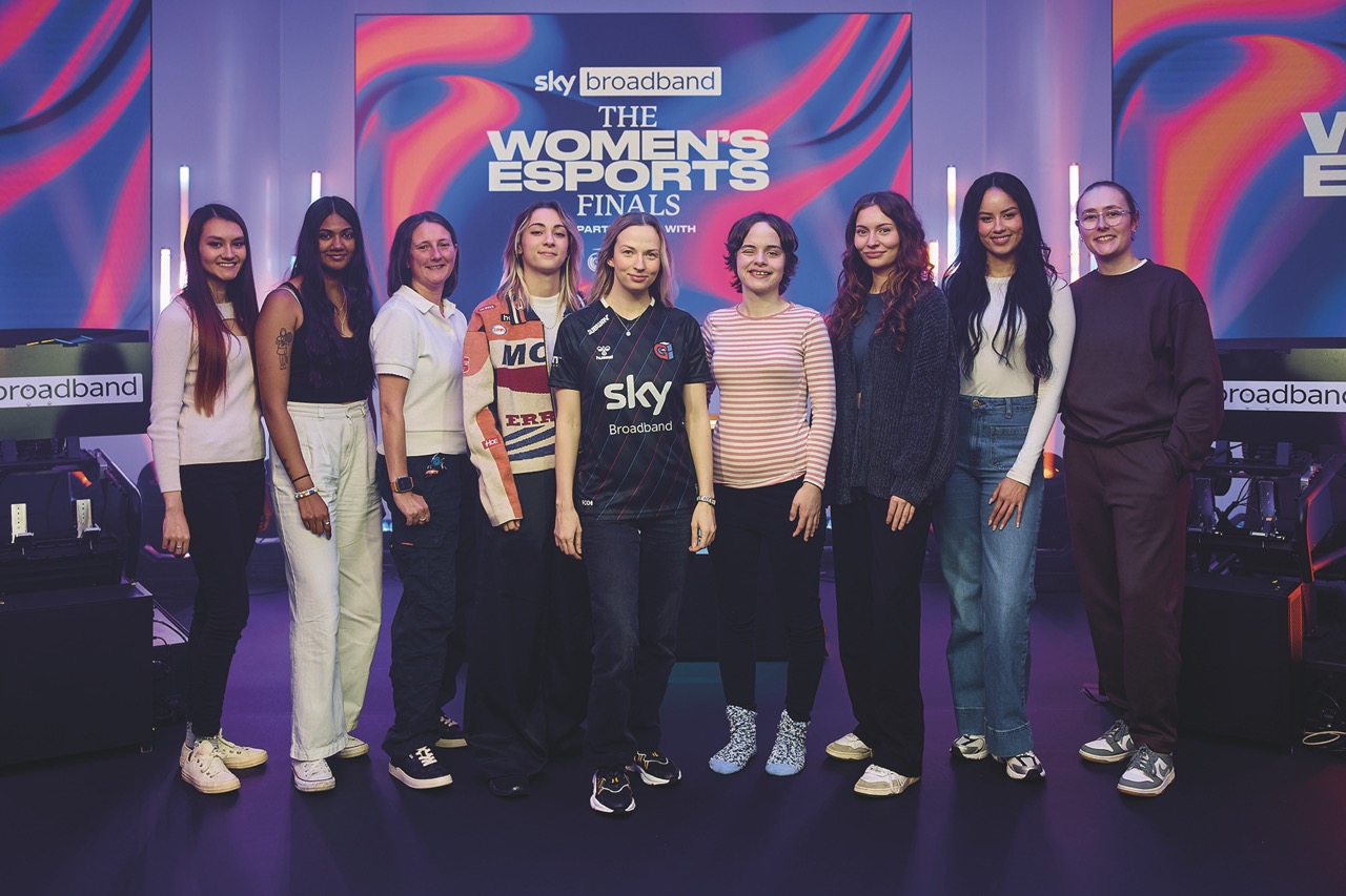 A row of women posing for a photo in front of a a banner for women's esports